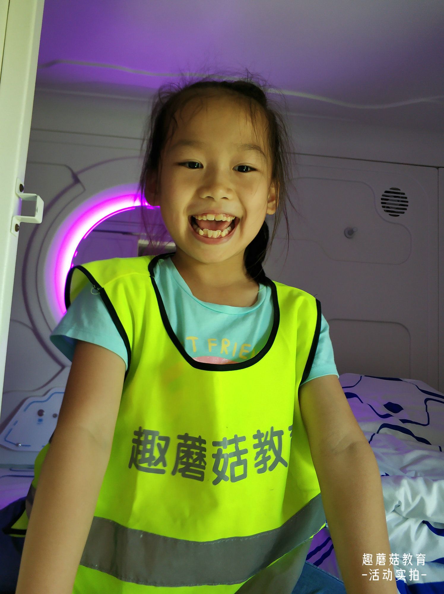 A girl in a green vest smiling inside a pod-style dorm room